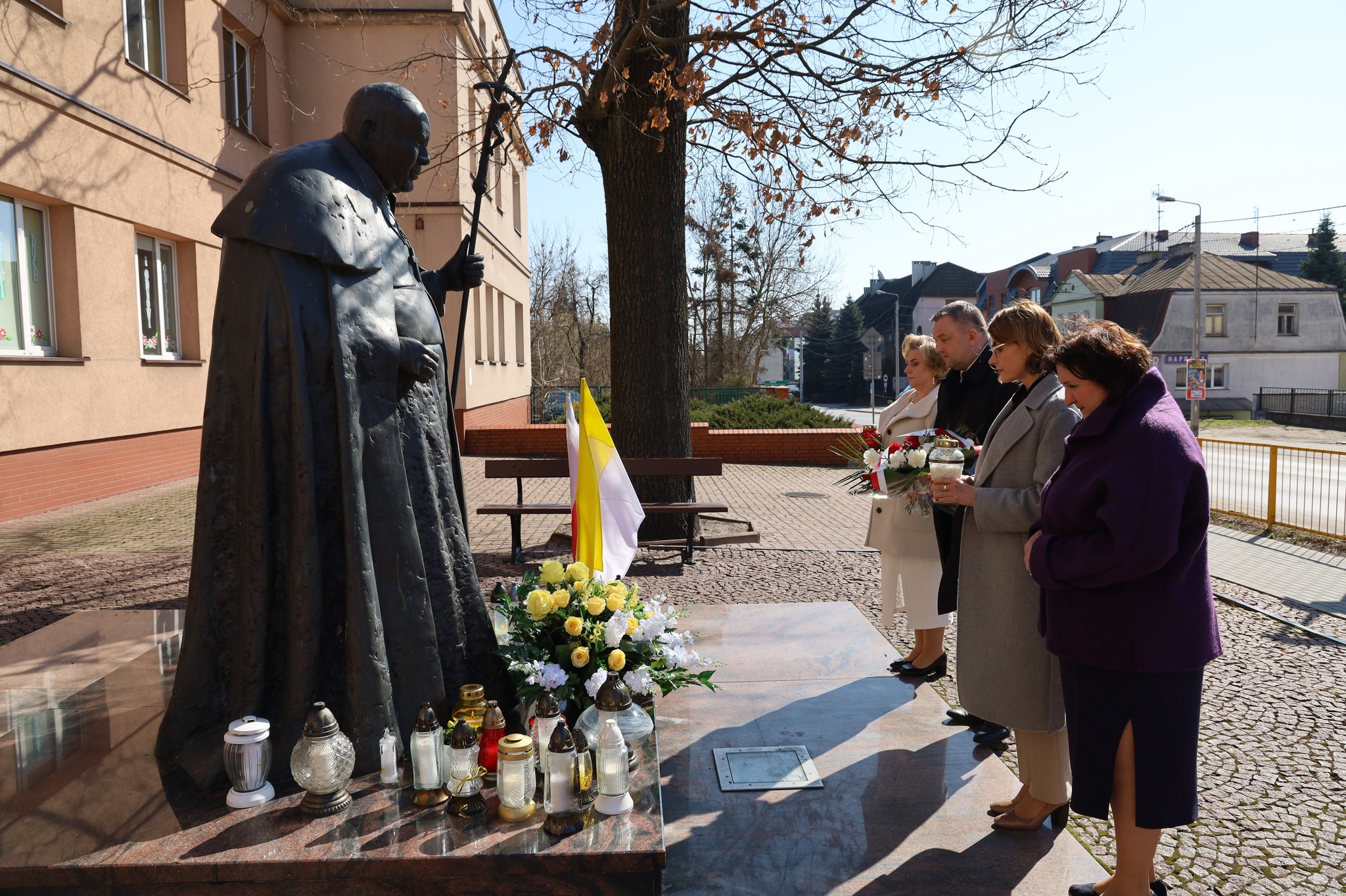 mężczyzna z 3 kobietami składa i zapala znicze pod pomnikiem